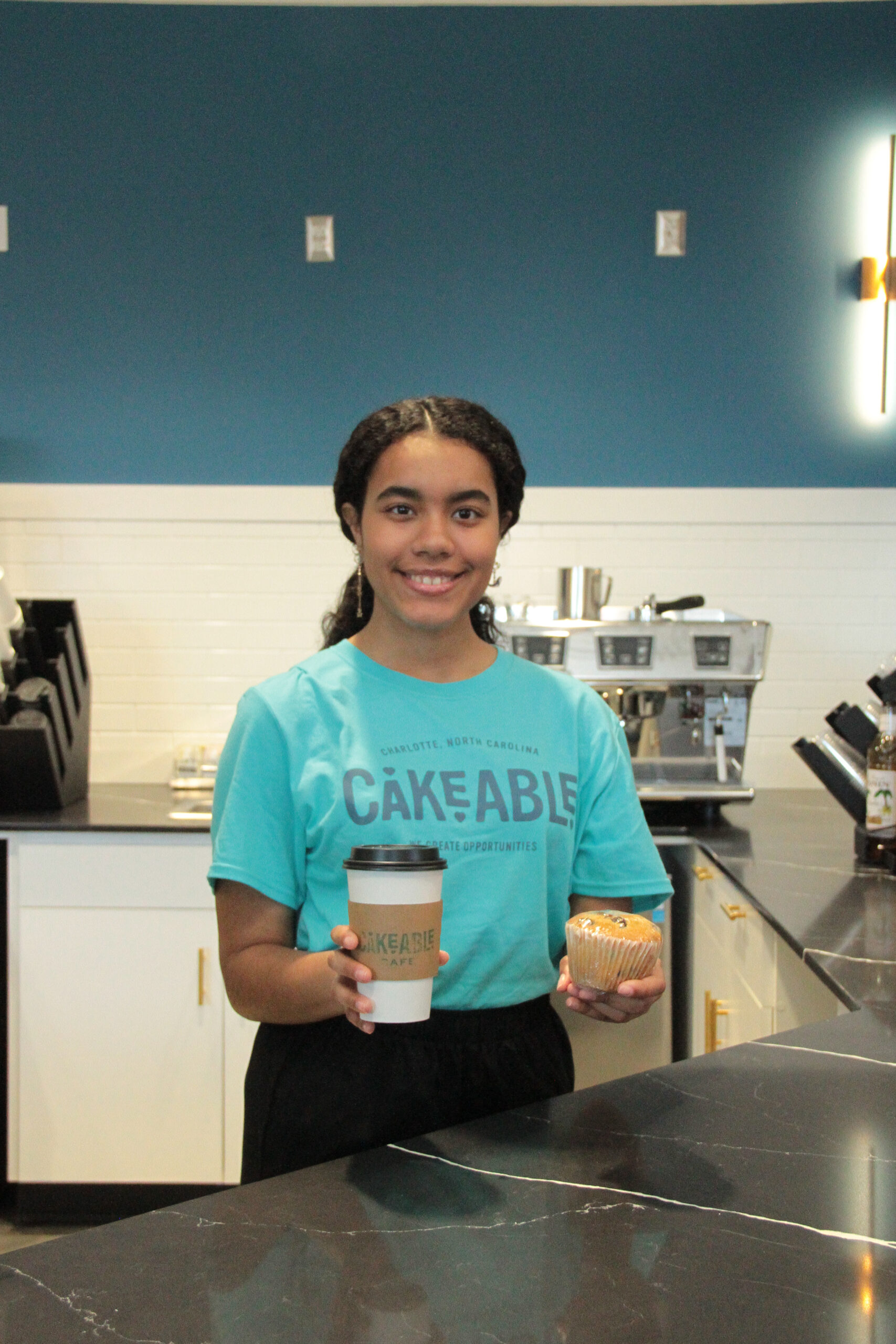 A Cakeable team member holding a coffee cup and a pastry behind the counter