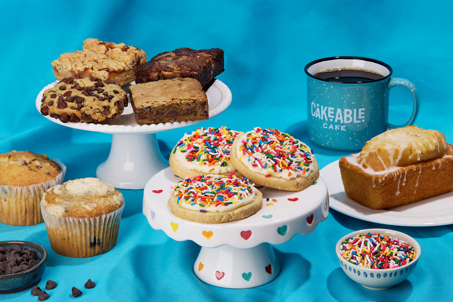An assortment of Cakeable baked goods - cookies, brownies, muffins and a loaf - beside a Cakeable Cafe mug