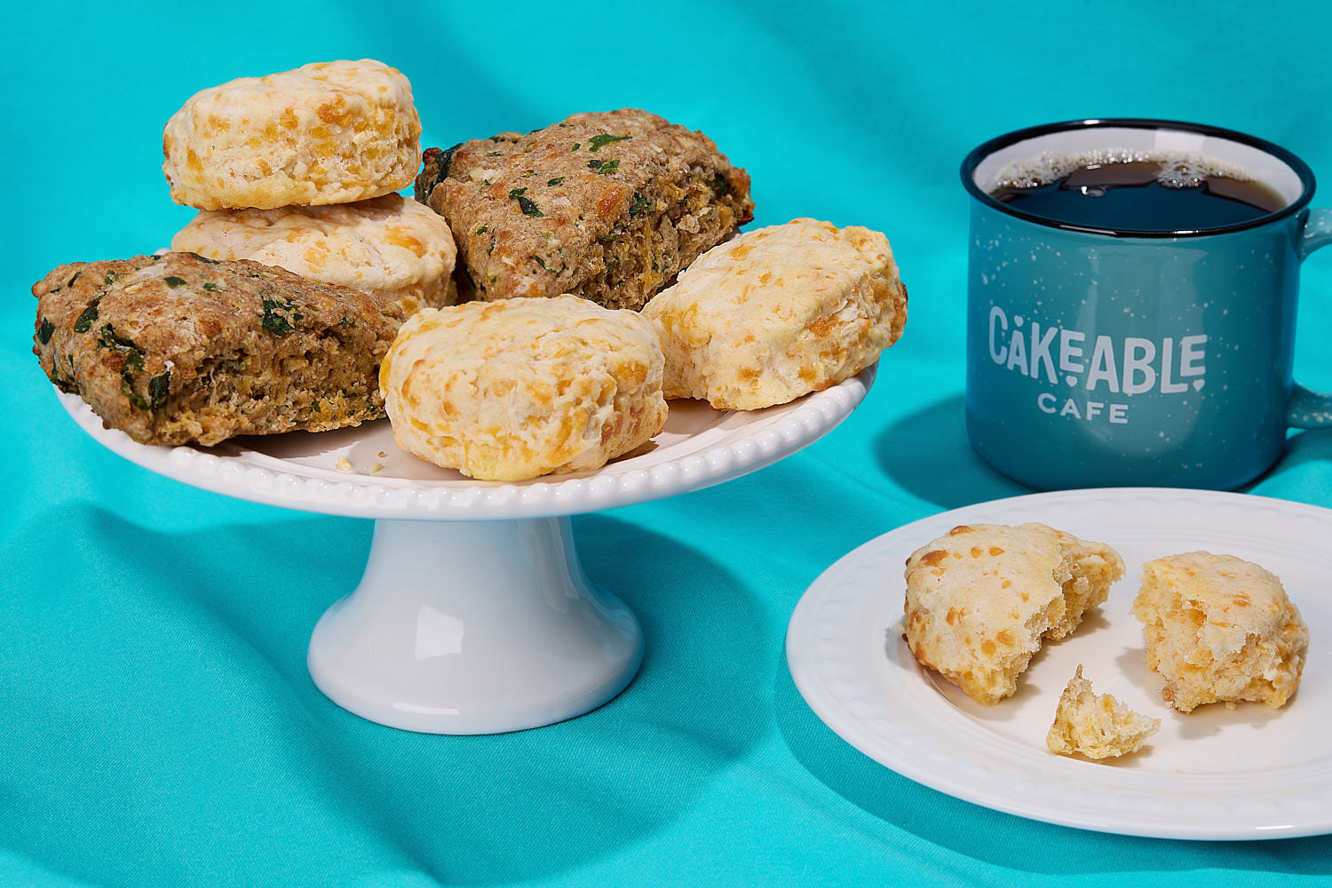 Cakeable scones and biscuits on a cake stand and plate beside a Cakeable Cafe mug