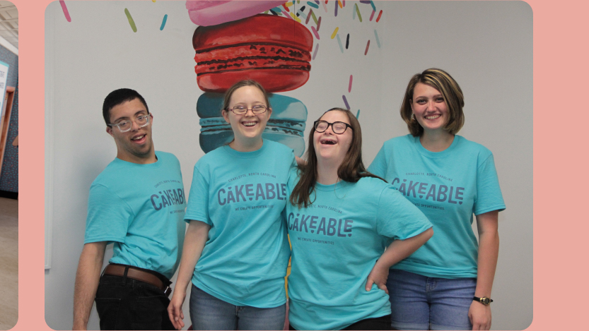 Four Cakeable team members in branded T-shirts laughing together in front of a macaron mural