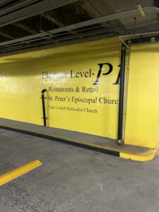 A parking deck wall lettered Elevator Level P1 for Restaurants and Retail, St. Peters Episcopal Church and First United Methodist Church