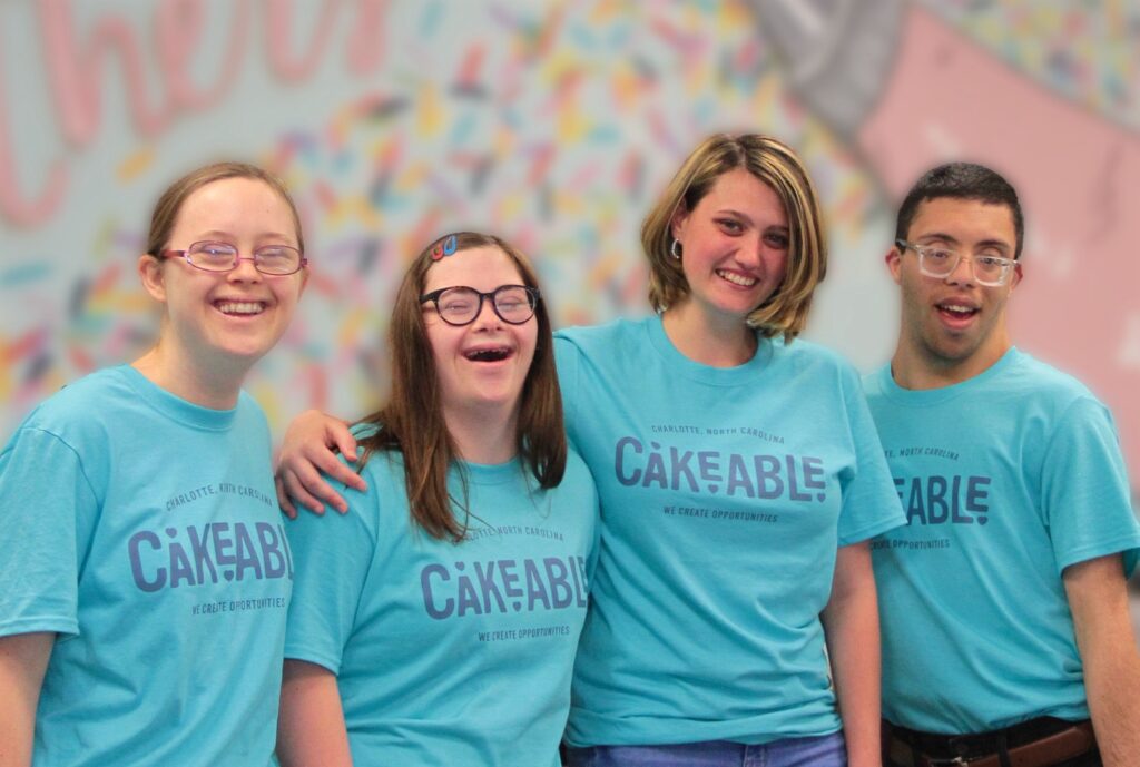 Four Cakeable team members in branded T-shirts smiling in front of a sprinkle mural