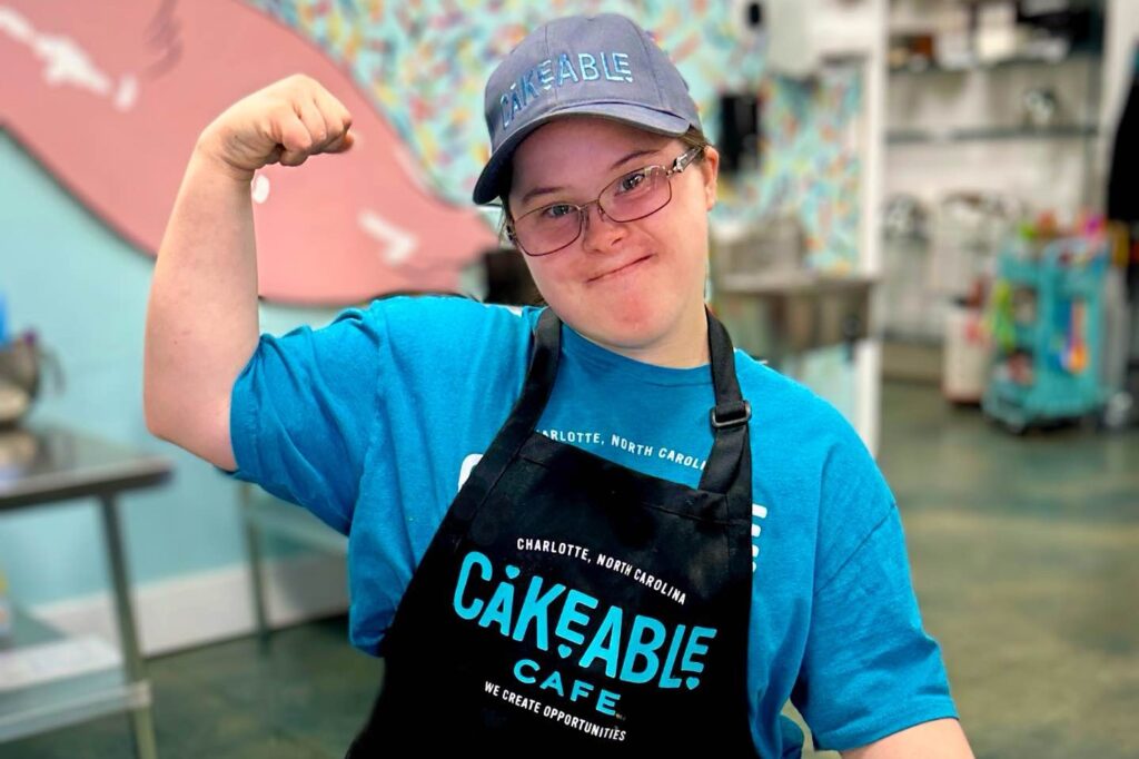 A Cakeable team member in a branded cap and apron flexing her arm and smiling
