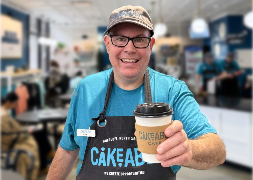 A Cakeable team member in a branded apron holding a Cakeable Cafe coffee cup