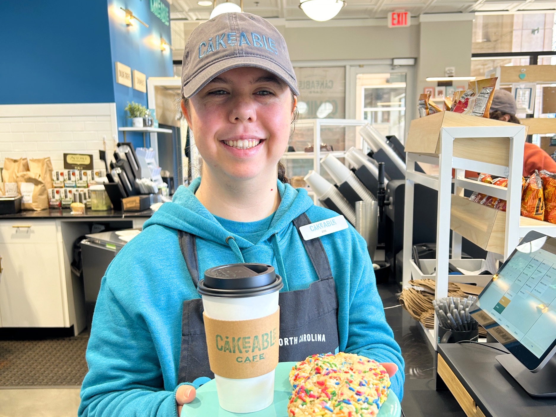 A Cakeable team member holding a coffee cup and a sprinkle-topped cookie