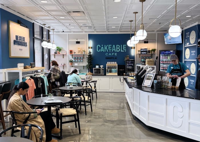 Customers seated at tables inside Cakeable Cafe, with the service counter and menu boards behind them