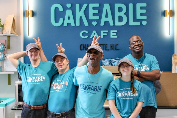 Five Cakeable team members laughing and making bunny-ear gestures under the Cakeable Cafe sign