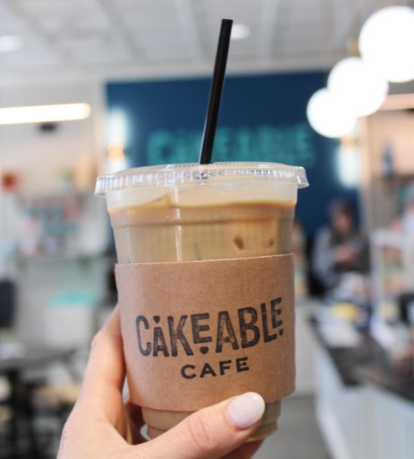 A hand holding a Cakeable Cafe iced coffee inside the cafe